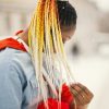 African American woman with vibrant braids poses in snowy urban environment.