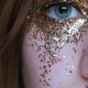 Close-up of a woman's eye adorned with shimmering gold glitter makeup.